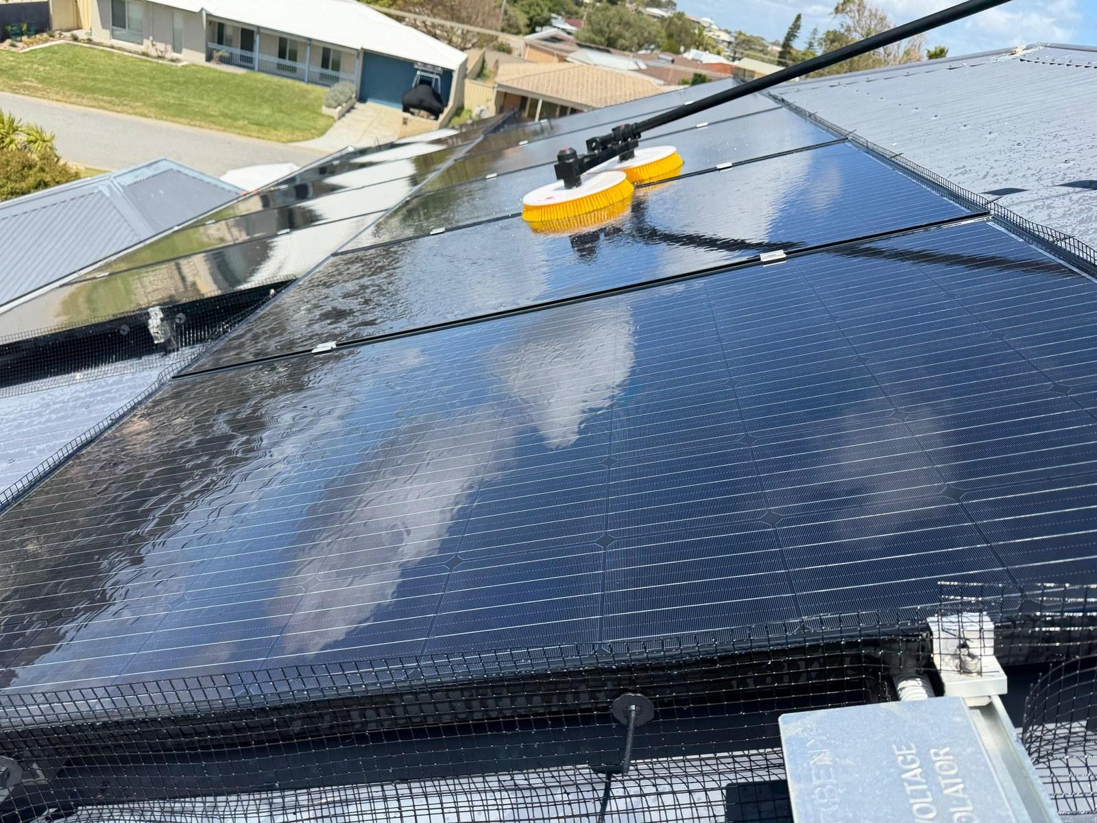 Rotating brush cleaning a solar array, sky reflected in the glass